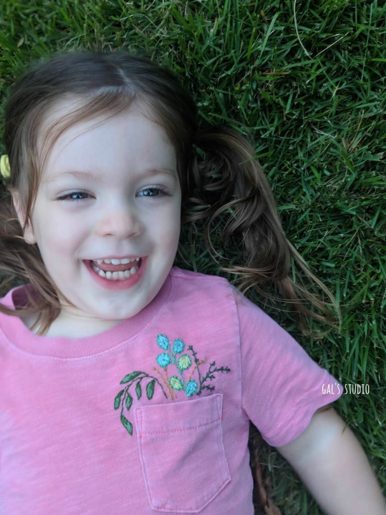 ילדה צוחקת בדשא עם חולצה רקומה בפרחים