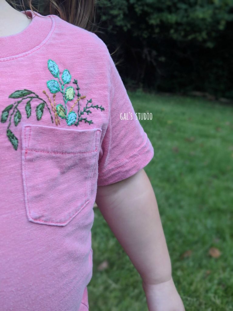 חולצה ורודה של ילדה עם רקמת פרחים בכיס